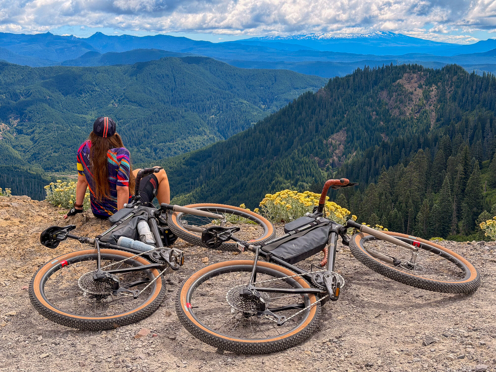 Two gravel bikes laid down at the Windy Ridge overlook with ranges receding beyond